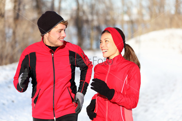 Couple running in winter snow living healthy lifestyle. Man and woman runner in their 20s. Young multi-ethnic couple, Asian woman, Caucasian man.