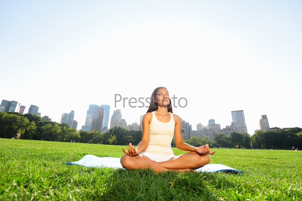 Meditating woman in meditation in New York City Central Park in yoga pose. Girl relaxing with serene relaxed expression outside in summer. Beautiful young mixed race Asian Caucasian female model.