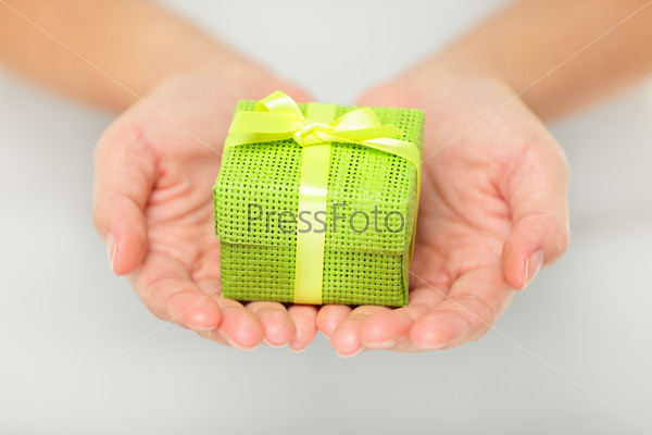 Small decorative colourful green gift held in outstretched cupped hands as a surprise Christmas present for a loved one