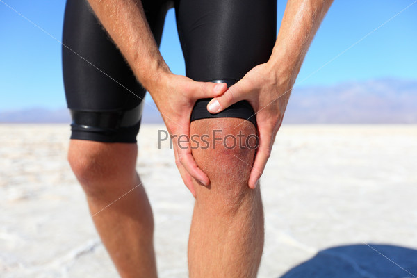 Injuries - sports running knee injury on man. Male runner with pain, maybe from sprain knee. Close up of legs, muscle and knee outdoors.
