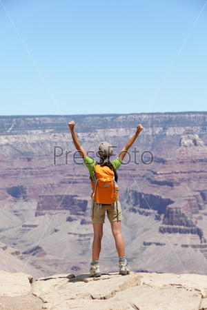 Happy hiker by Grand Canyon south rim cheering happy with arms raised up enjoying the beautiful scenic landscape. Hiking woman wearing backpack and outdoor outfit. Summer in Grand Canyon, Arizona, USA