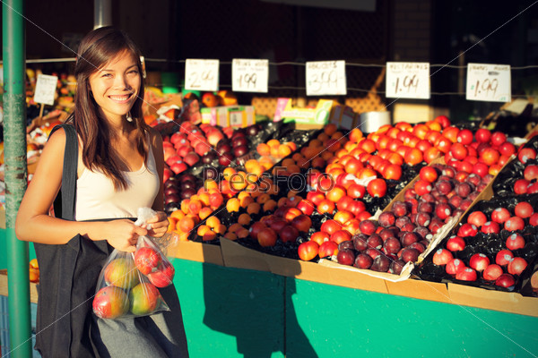 Woman buying fruits and vegetables at farmers market. Candid portrait of young woman shopping for healthy lifestyle. Multiracial Asian Caucasian female model.
