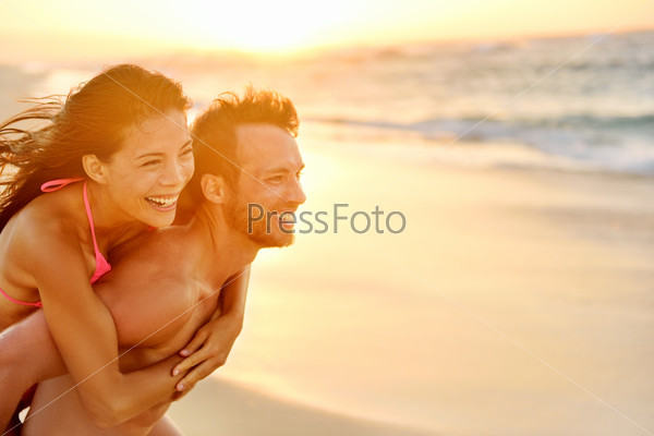 Lovers couple in love having fun piggybacking on date on beach. Portrait beautiful healthy young adults girlfriend and boyfriend hugging happy. Multiracial dating or healthy relationship. From Hawaii.