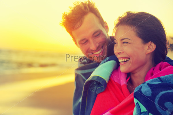 Bathing romantic couple with towel on beach sunset. Portrait of happy young interracial couple embracing each other having fun outdoors during holidays vacation travel. Asian woman, Caucasian man.