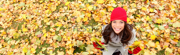Autumn / fall banner background texture of leaves with happy woman. Panoramic fall concept portrait of smiling excited girl sitting on colorful autumn leaves outdoor in forest. Mixed race Asian girl.