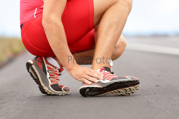 Broken twisted ankle - running sport injury. Male runner touching foot in pain due to sprained ankle.