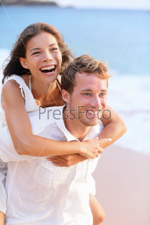 Happy couple piggybacking on beach.