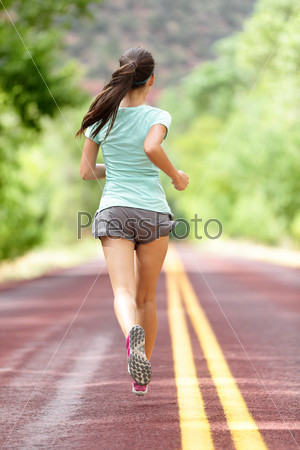 Young lady working out running away on rural road. Woman runner athlete training jogging during workout outside. Full body length rear view showing back. Girl in shorts and running shoes.
