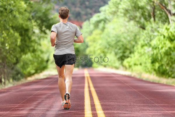 Male runner running on road training for fitness. Man doing jogging workout run outside in summer in nature. Athlete in running shoes and shorts working out for marathon.