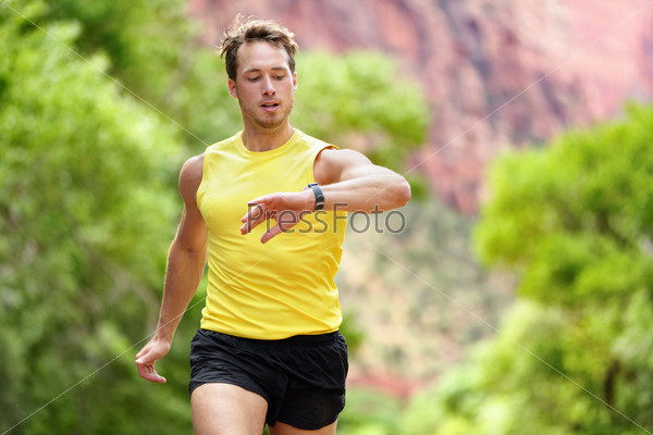 Runner looking at heart rate monitor smartwatch while running. Man jogging outside looking at his sports smart watch during workout training for marathon run. Fit male fitness model in his 20s.