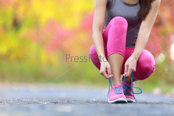 Running shoes - woman tying shoe laces. Closeup of female sport fitness runner getting ready for jogging outdoors on forest path in late summer or fall.