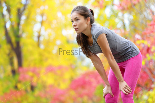 Athlete runner resting after running - Asian woman. and jogging training outdoors in forest. Tired exhausted beautiful sports fitness model living healthy active lifestyle. Mixed race Asian Caucasian.