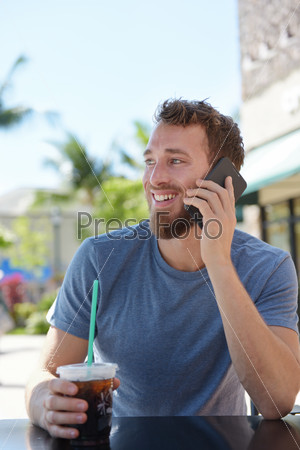 Man on cafe using smartphone talking on mobile cell smart phone drinking iced coffee in summer. Handsome young casual man using smartphone smiling happy sitting outdoors. Urban male in his 20s.
