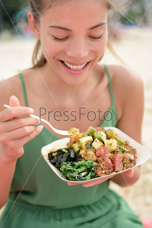 Woman eating local Hawaii food dish Poke bowl salad. Girl enjoying healthy lunch - a traditional local Hawaiian dish with raw marinated ahi yellowfin tuna fish. Healthy lifestyle concept.