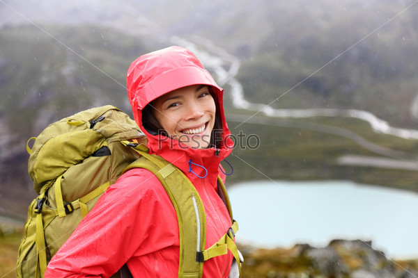 Hiker woman hiking with backpack in rain on trek living healthy life. Smiling fresh and candid young asian girl walking on hike in mountain nature landscape while raining in Swiss alps, Switzerland.