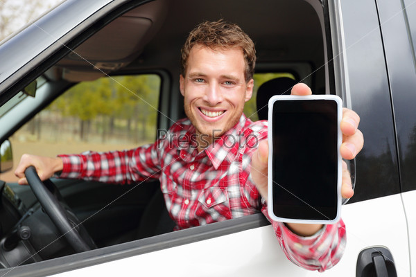 Smartphone man driving car showing app on screen display smiling happy. Male driver using 4g apps showing blank empty touchscreen sitting in drivers seat. Focus on model and on screen for copy space.