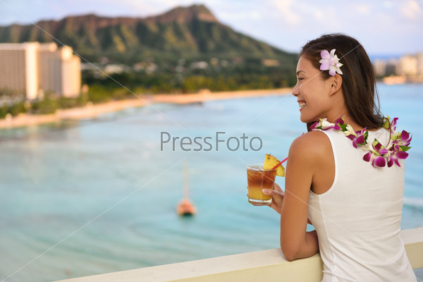 Hawaiian woman drinking Mai Tai in resort on Waikiki beach, Hawaii. Beautiful Asian tourist on Hawaii travel looking at sunset over Diamond Head mountain in Honolulu, Oahu, Hawaii USA.