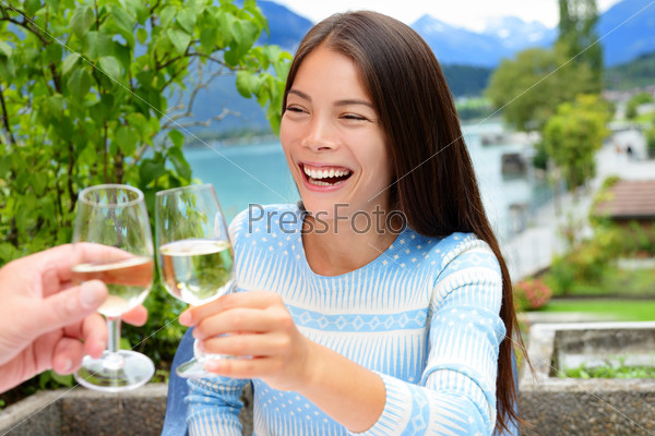 Couple toasting wine glass at outdoor restaurant. Asian woman cheering with alcohol drink in Swiss Alps, Switzerland in summer at outside terrace near lake.