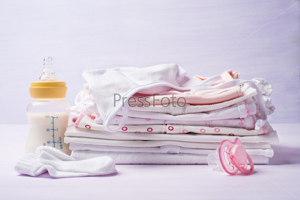 Pile of children\'s clothing with a bottle of milk and pacifier, close-up