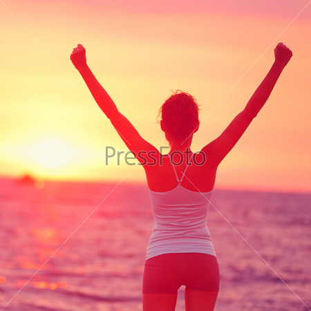 Life achievement - happy woman arms up in success. Back view of female silhouette proud of reaching her health goal arms raised looking at ocean and sunset. Happiness winning goal concept.
