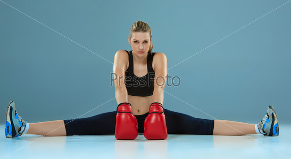 beautiful  boxer girl with the red gloves is sitting in twine on gray background