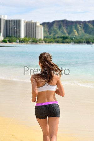 Active fit female sport runner jogging on beach. Woman jogger from behind working out her cardio by running on sunny Waikiki beach, Honolulu city, Oahu island, Hawaii, USA.