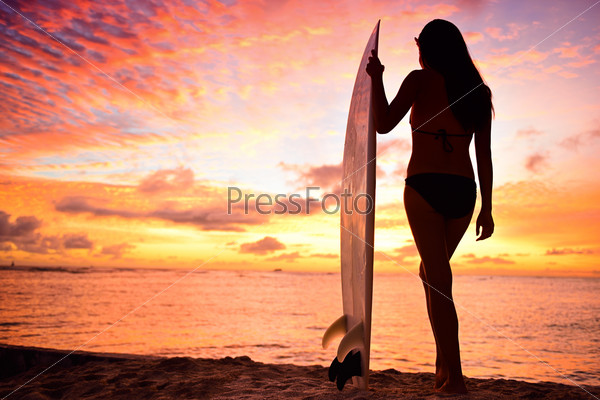 Surfer girl surfing looking at ocean beach sunset. Silhouette of female bikini woman looking at water with standing with surfboard having fun living healthy active lifestyle. Water sports with model.