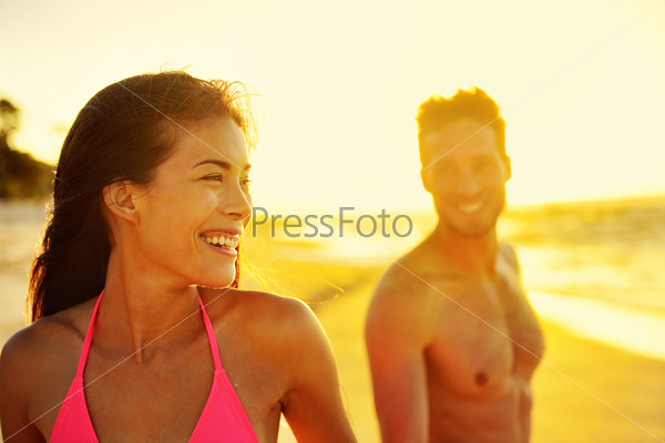 Happy multicultural couple on beach vacations. Hawaii in sunset, young healthy adults together laughing walking in summer day. Asian mixed race woman, Caucasian man.