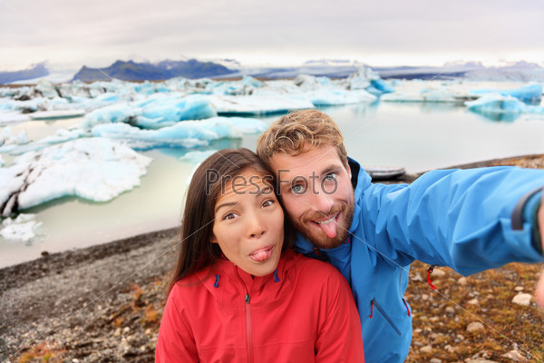 Funny selfie couple taking self portrait photograph on Iceland having fun on travel by Jokulsarlon glacial lagoon / glacier lake. Tourists enjoying beautiful Icelandic nature landscape Vatnajokull.