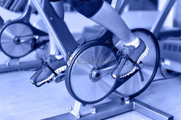 Exercise bike with spinning wheels. Woman excising biking in fitness center. closeup of pedals. Professional fitness center equipment.