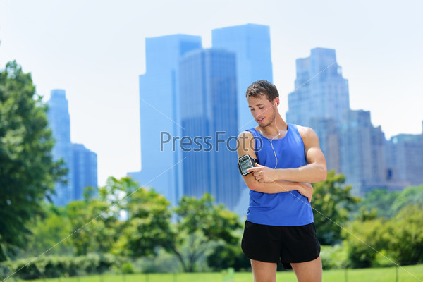 New York City man runner listening music on smartphone. Male adult jogger running using touchscreen on armband for workout in Central Park with urban background of Manhattan\'s skyscrapers skyline.