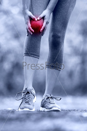 Knee injury - runner with sprained leg joint pain. Closeup of female athlete\'s leg with red circle showing pain. Woman holding with hands around hurting knee in summer nature background.