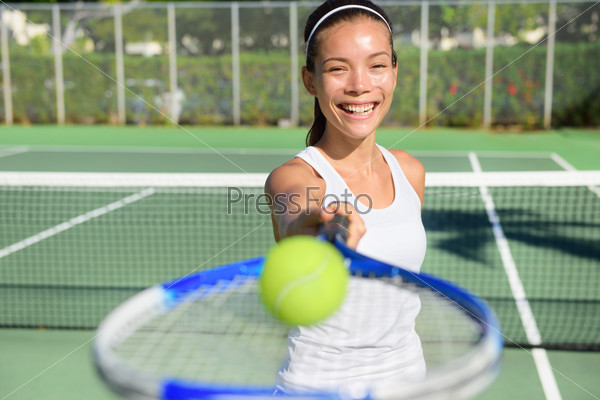 Tennis player portrait. Woman showing tennis ball and racket smiling happy. Female athlete inviting you to play tennis. Healthy active sport and fitness lifestyle concept outdoor.