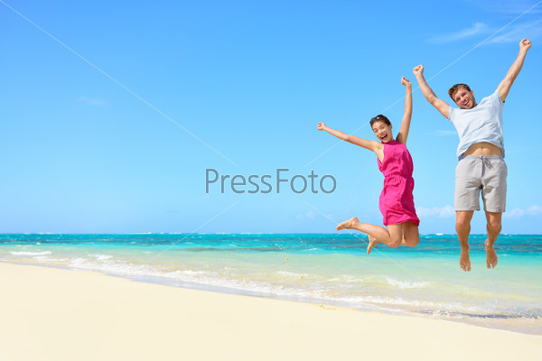 Happy couple tourists jumping on beach vacations. Travel concept of young couple cheering for summer holidays showing success, happiness, and joy on perfect white sand tropical beach under the sun.
