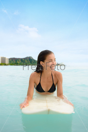 Surf woman surfing on surfboard in Waikiki, Hawaii. Beautiful portrait of Asian girl waiting for waves in ocean lying down on surf board in Hawaiian city, Honolulu, Oahu, Hawaii, USA.