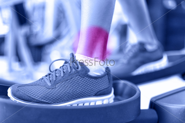 Hurting ankles - pain caused by fitness injury. Closeup of leg with red circle showing painful area of female athlete training on elliptical exercise machine. Sprained ankle concept.