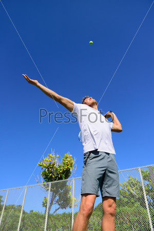Tennis player serving playing outdoors sport. Man serve with throwing tennis ball up. Male athlete training practicing outdoors in summer.