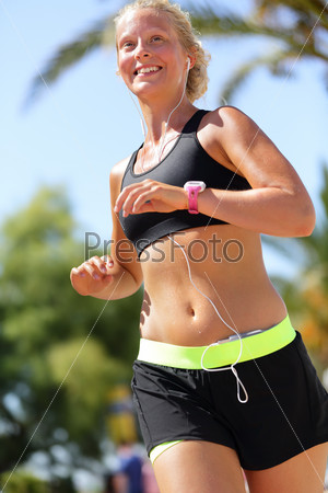 Happy female marathon runner running listening music with earphones on smartphone and wearing a tech smartwatch activity tracker or a heart rate monitor sportswatch. Fitness woman exercising cardio.