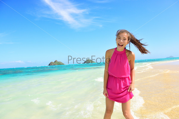 Woman having fun portrait on Hawaii Lanikai beach. Young mixed race female by water wearing pink sundress laughing during summer travel holidays on Oahu, Hawaii, USA with Mokulua Islands.