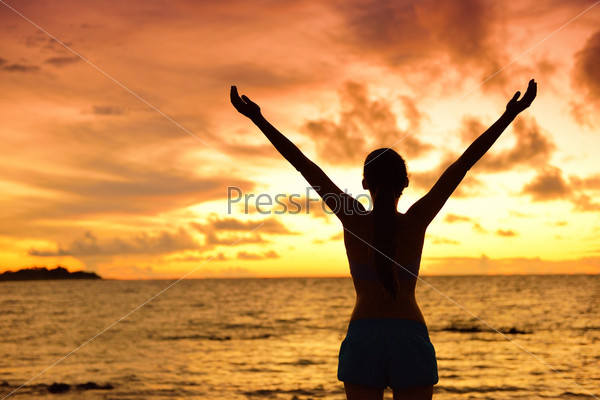 Freedom woman silhouette living healthy lifestyle a happy carefree and free life. Portrait from the back of an unrecognizable female adult at beach holidays in sunset with arms raised up in the sky.