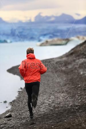 Runner man trail running training for run in beautiful nature landscape. Fit male athlete jogging and cross country running by icebergs in Jokulsarlon glacial lake in Iceland.