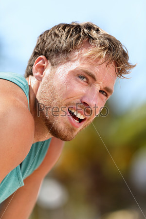 Tired male runner catching breath during marathon training. Running male adult taking a break and breaking a sweat after a run under the sun. Fitness athlete exhausted breathing with difficulty.