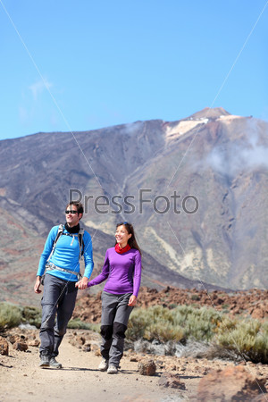 Couple hiking outdoors in nature. Happy young couple hikers walking outside in dramatic mountain landscape on volcano Teide, Tenerife, Canary Islands.