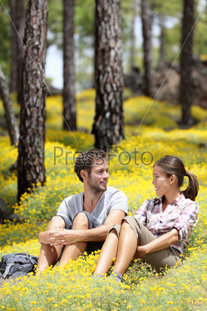 Happy couple in forest sitting smiling around flowers. Beautiful young couple: Asian woman, Caucasian man. Photo from Tenerife, Spain.