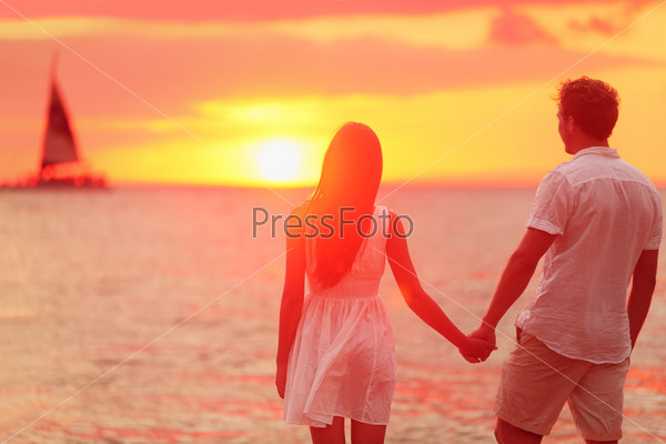 Honeymoon couple romantic in love holding hands at beach sunset. Newlywed happy young couple enjoying ocean sunset during travel holidays vacation getaway. Interracial couple.