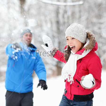 Winter fun - couple in snowball fight having fun together in forest snow landscape. Happy young interracial couple playing together in the snow.