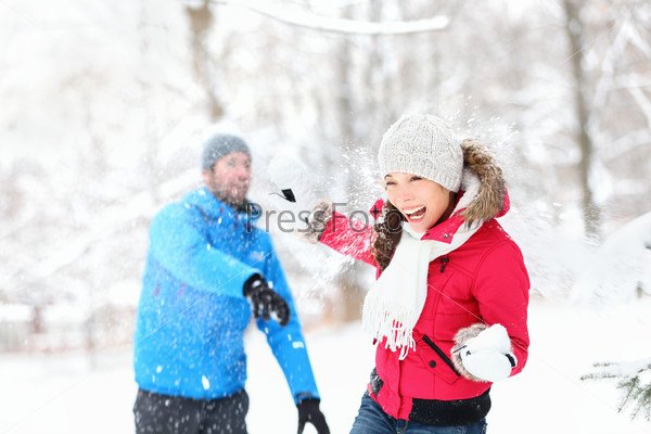 Snowball fight. Winter couple having fun playing in snow outdoors. Young joyful happy multi-racial couple.