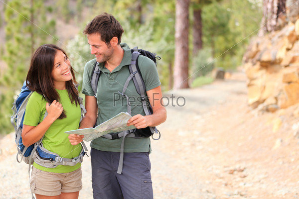 Happy couple hiking looking at map. Young interracial couple hikers smiling happy walking in forest during spring or summer. Asian woman, Caucasian man.