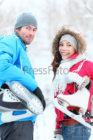 Ice skating winter couple smiling happy holding ice skates outdoors. Beautiful young couple, Asian woman, Caucasian man outside on snow winter day.