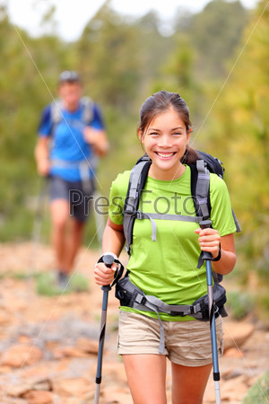Hiker woman. Hiking asian woman walking with hiking poles and hiking backpack smiling happy outdoors in nature. Hiker in background.